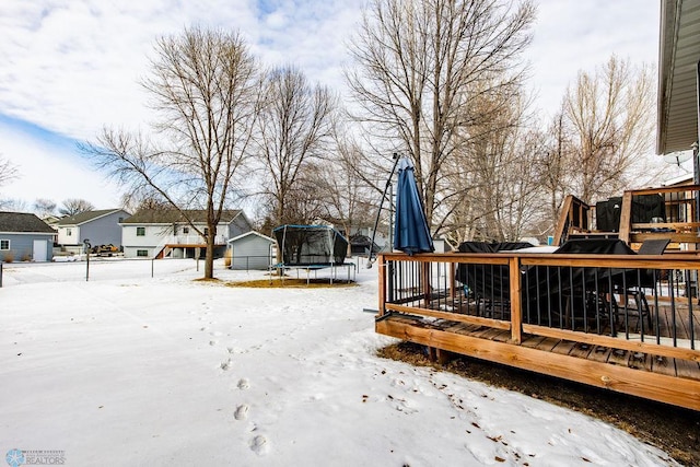 yard layered in snow with a wooden deck and a trampoline