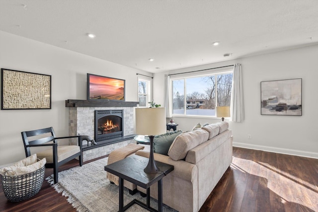 living area with recessed lighting, baseboards, a warm lit fireplace, and wood finished floors