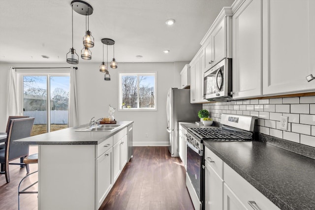 kitchen featuring dark countertops, backsplash, appliances with stainless steel finishes, and a kitchen island with sink