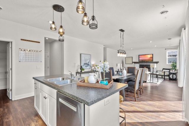 kitchen featuring dark countertops, dark wood-style flooring, stainless steel dishwasher, and a sink