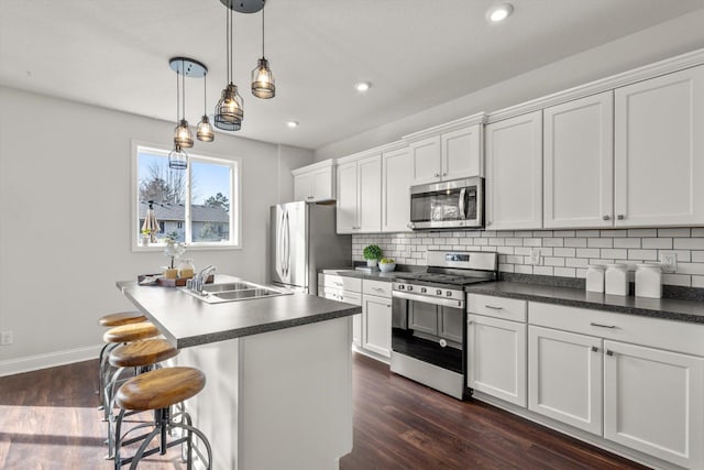 kitchen featuring dark wood-style flooring, a sink, appliances with stainless steel finishes, dark countertops, and backsplash