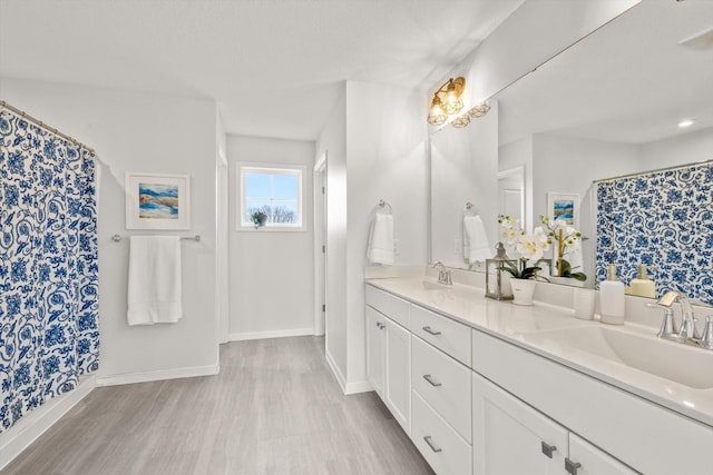 bathroom featuring double vanity, wood finished floors, baseboards, and a sink