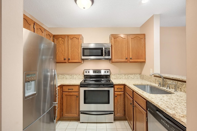 kitchen with sink, light tile patterned floors, appliances with stainless steel finishes, light stone countertops, and a textured ceiling