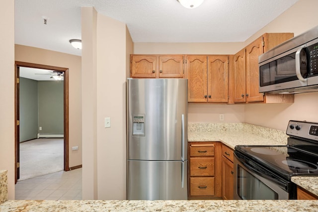 kitchen with appliances with stainless steel finishes, a baseboard heating unit, light tile patterned floors, and a textured ceiling