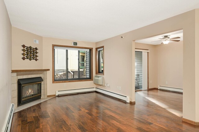 unfurnished living room featuring hardwood / wood-style flooring, a fireplace, a wall unit AC, and a baseboard heating unit