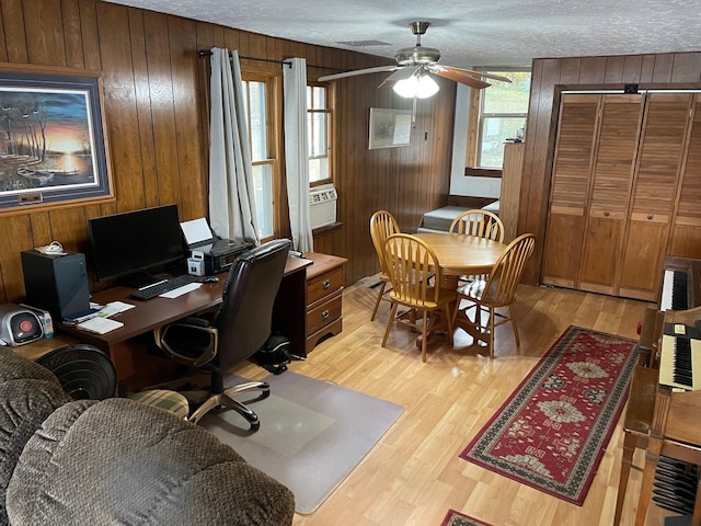 office featuring ceiling fan, light hardwood / wood-style flooring, a textured ceiling, and wood walls