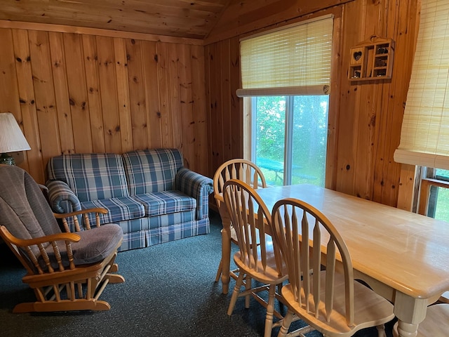 carpeted dining area featuring wooden walls and vaulted ceiling