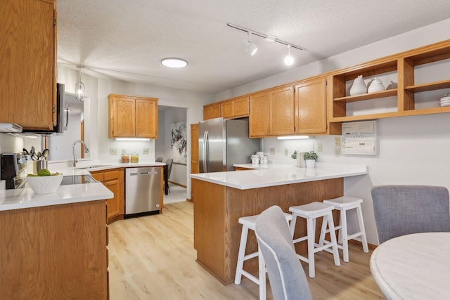 kitchen with sink, stainless steel appliances, a textured ceiling, kitchen peninsula, and light wood-type flooring