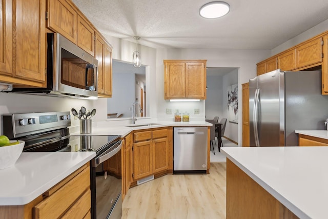 kitchen with sink, stainless steel appliances, a textured ceiling, decorative light fixtures, and light wood-type flooring