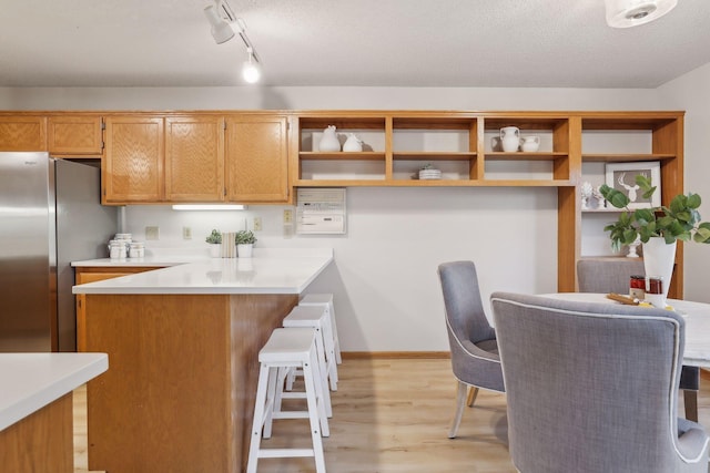 kitchen featuring light hardwood / wood-style flooring, stainless steel fridge, track lighting, a textured ceiling, and a kitchen bar