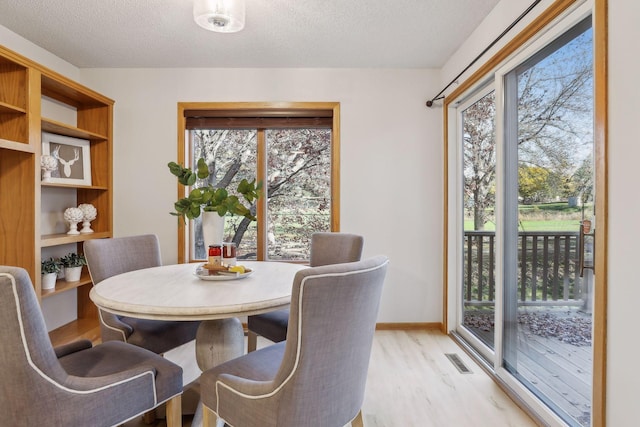 dining area with a wealth of natural light, a textured ceiling, and light wood-type flooring