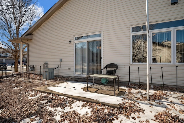 snow covered back of property featuring central air condition unit and a patio area