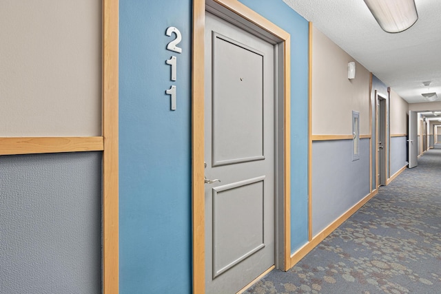 hallway with dark colored carpet and a textured ceiling