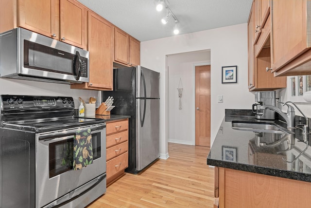 kitchen featuring sink, a textured ceiling, dark stone countertops, stainless steel appliances, and light hardwood / wood-style floors