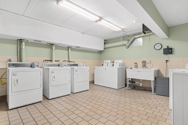 clothes washing area featuring tile walls, sink, and washing machine and dryer