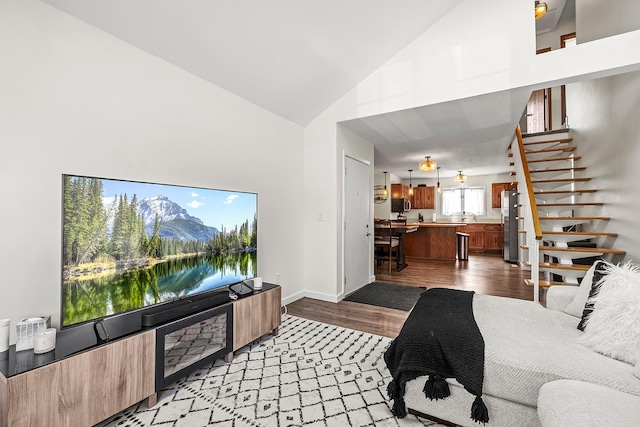 living room featuring light wood-type flooring, stairway, baseboards, and high vaulted ceiling