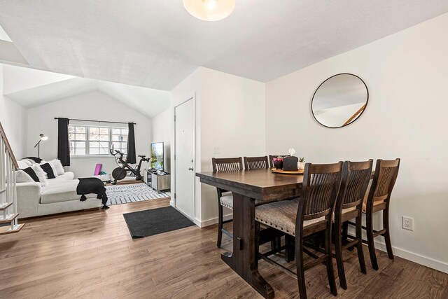 dining space featuring wood finished floors, vaulted ceiling, and baseboards