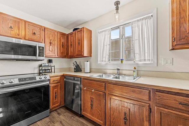 kitchen with appliances with stainless steel finishes, a sink, light countertops, and brown cabinets