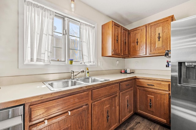 kitchen featuring stainless steel refrigerator with ice dispenser, a sink, brown cabinetry, light countertops, and dark wood-style flooring