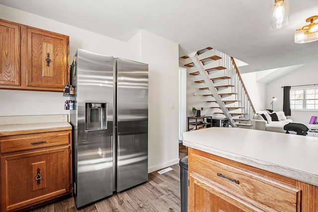 kitchen with stainless steel fridge, light countertops, brown cabinetry, light wood-style floors, and open floor plan