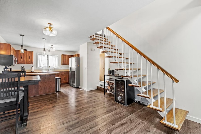 kitchen with stainless steel refrigerator with ice dispenser, dark wood-type flooring, brown cabinetry, decorative light fixtures, and baseboards