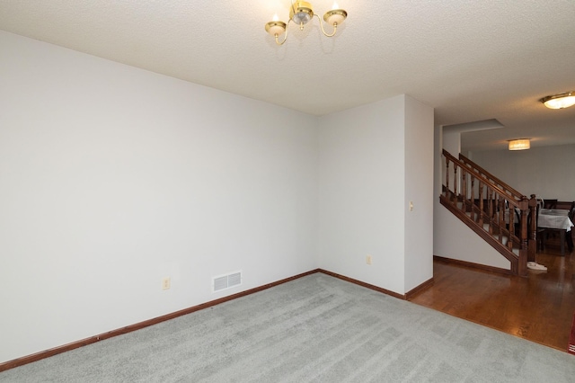 carpeted spare room featuring a notable chandelier and a textured ceiling