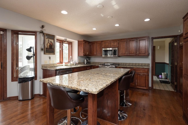 kitchen with a breakfast bar, sink, a center island, dark hardwood / wood-style flooring, and light stone countertops