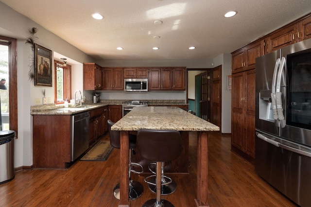 kitchen with appliances with stainless steel finishes, light stone counters, a textured ceiling, a kitchen island, and dark hardwood / wood-style flooring