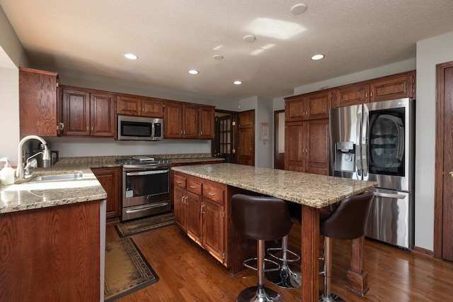 kitchen featuring a kitchen island, dark hardwood / wood-style floors, sink, light stone counters, and stainless steel appliances