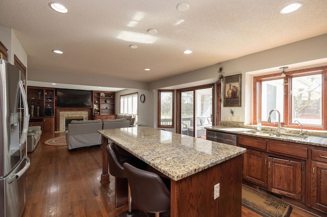 kitchen with a kitchen island, appliances with stainless steel finishes, a fireplace, dark hardwood / wood-style flooring, and light stone counters