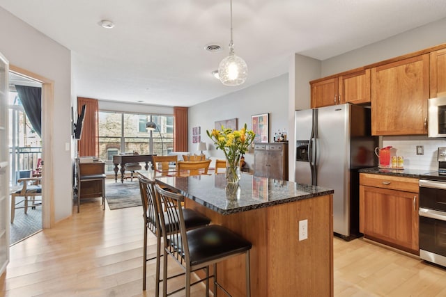 kitchen with stainless steel appliances, light wood-style floors, a kitchen island, and tasteful backsplash