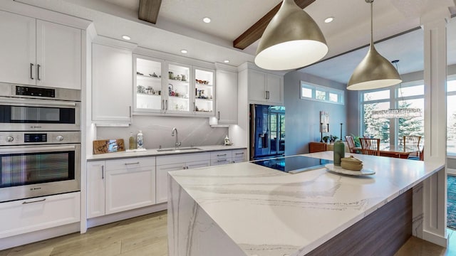 kitchen featuring fridge with ice dispenser, sink, decorative light fixtures, stainless steel double oven, and white cabinets