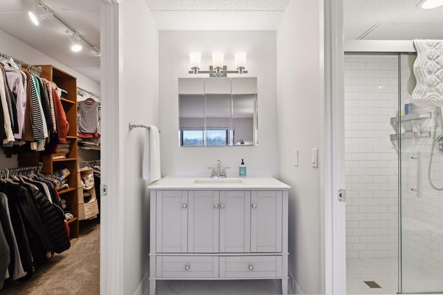 bathroom with a spacious closet, a shower stall, a textured ceiling, and vanity