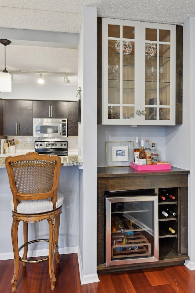 bar featuring beverage cooler, dark wood-style floors, appliances with stainless steel finishes, a dry bar, and tasteful backsplash