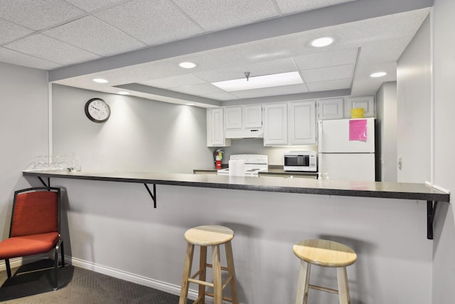 kitchen featuring under cabinet range hood, white appliances, carpet, and a breakfast bar