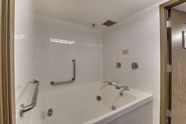 full bath with a tub with jets, a textured ceiling, and tile walls