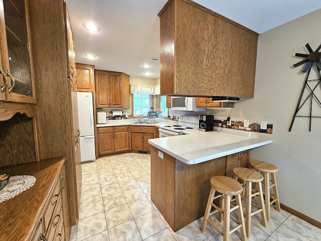 8785 Ilex Pl NW, Rice, MN 56367 - kitchen featuring white appliances, brown cabinetry, a peninsula, a sink, and a breakfast bar