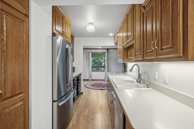 kitchen with appliances with stainless steel finishes, sink, and light hardwood / wood-style floors