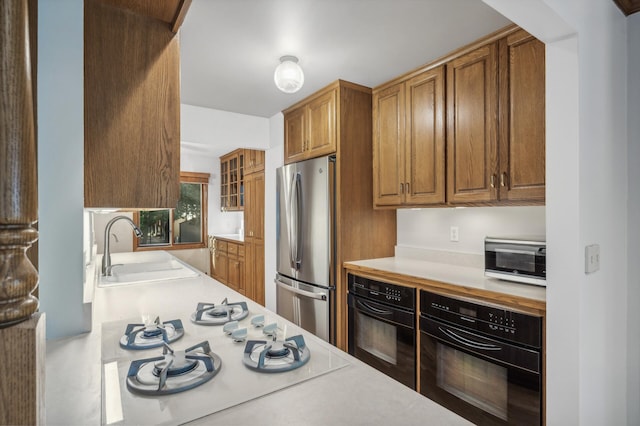 kitchen featuring stovetop, sink, stainless steel fridge, and black oven