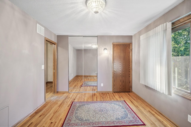 unfurnished bedroom with multiple windows, a textured ceiling, and light wood-type flooring