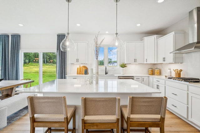 kitchen featuring pendant lighting, wall chimney range hood, white cabinetry, a center island, and stainless steel gas stovetop