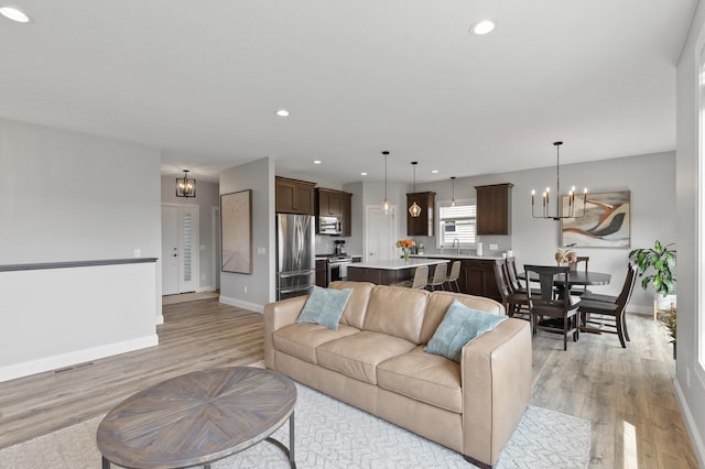 living room featuring sink, light wood-type flooring, and a notable chandelier