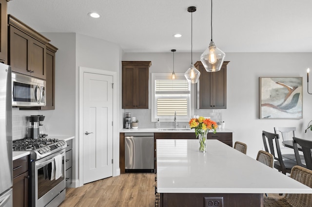 kitchen with pendant lighting, stainless steel appliances, a kitchen bar, and sink