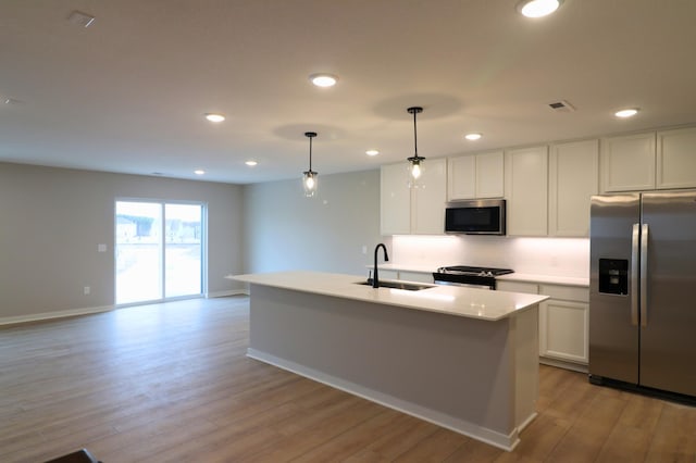 kitchen featuring sink, appliances with stainless steel finishes, a kitchen island with sink, hanging light fixtures, and white cabinetry