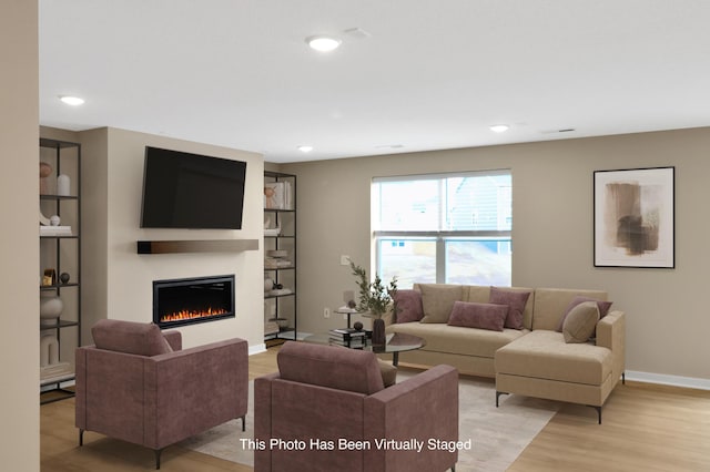 living room with a glass covered fireplace, baseboards, light wood finished floors, and recessed lighting