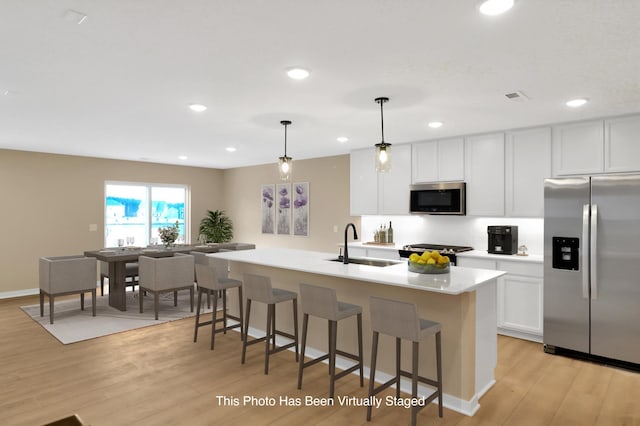 kitchen featuring a center island with sink, stainless steel appliances, light countertops, hanging light fixtures, and a sink