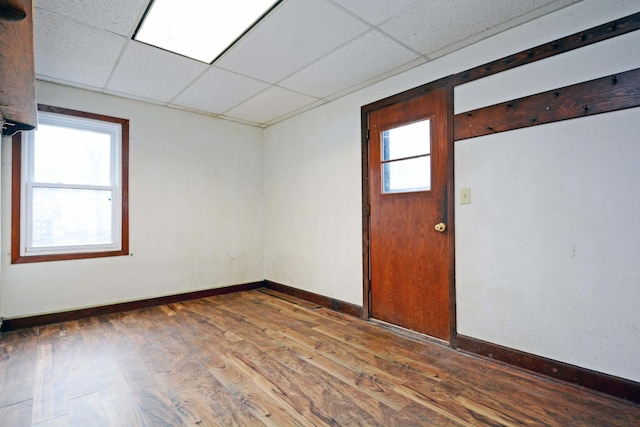 spare room with a drop ceiling, wood-type flooring, and a healthy amount of sunlight