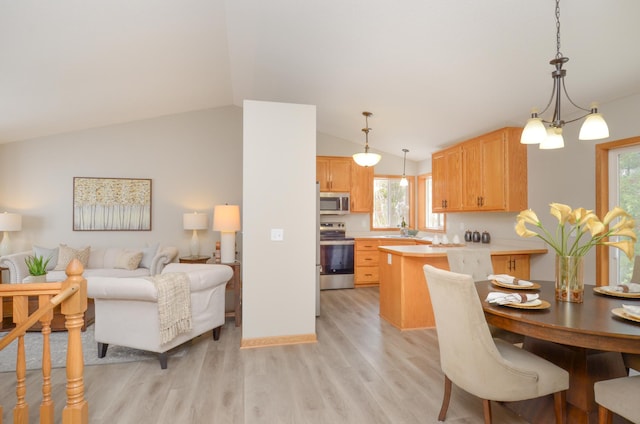 kitchen featuring lofted ceiling, hanging light fixtures, stainless steel appliances, light hardwood / wood-style floors, and light brown cabinets