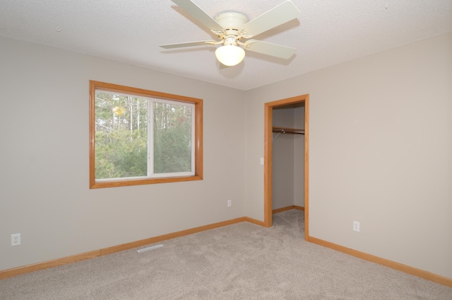 unfurnished bedroom featuring a spacious closet, light carpet, a textured ceiling, a closet, and ceiling fan