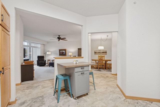 kitchen featuring a breakfast bar area, ceiling fan, hanging light fixtures, a center island, and light carpet